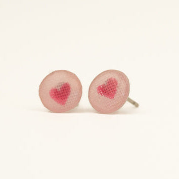 Pair of earrings with pink heart designs on a light pink background
